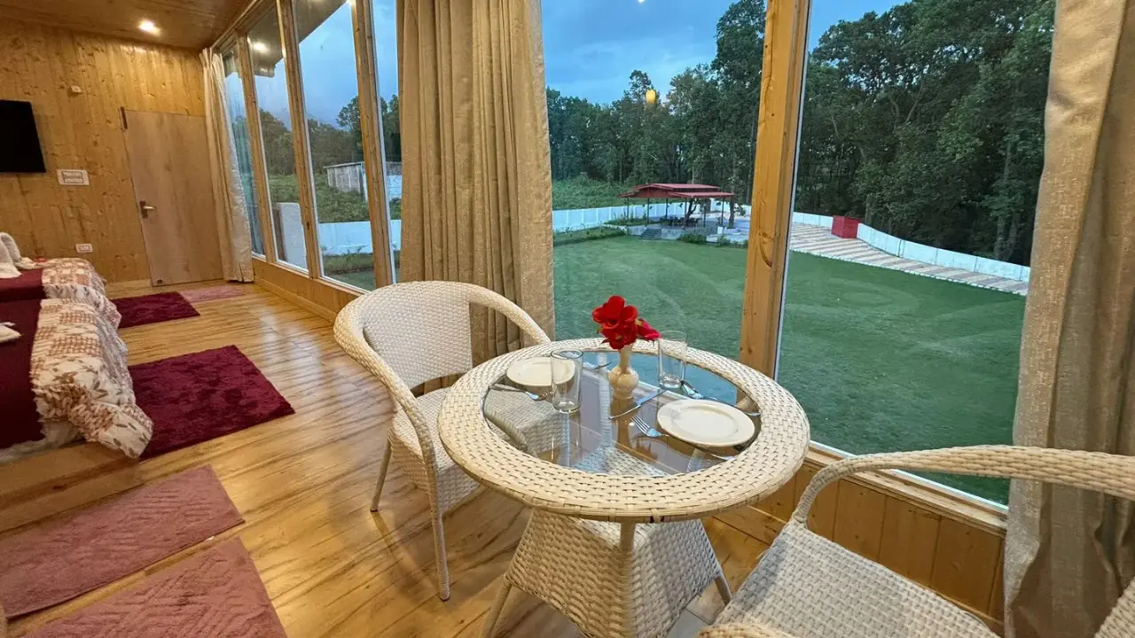 Romantic couple seating inside pinewood cottage with glass walls overlooking garden at Pristine Woods, best resort in Dehradun for couples