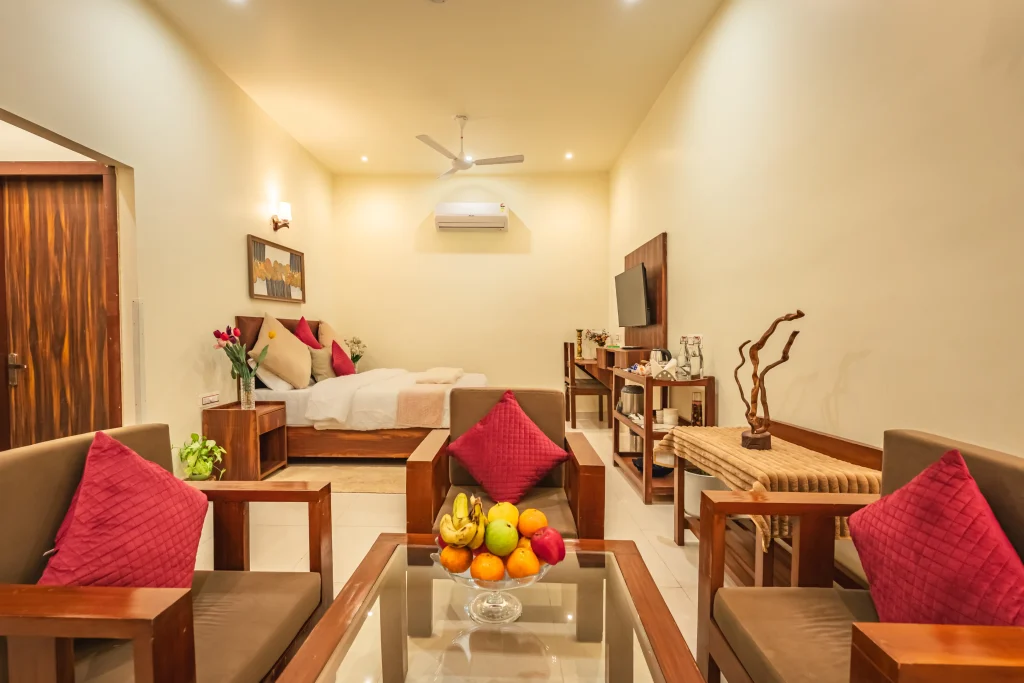 Premium deluxe room with cosy seating area at Pristine Woods, the Luxury Resort in Dehradun, featuring a king-size bed, elegant wooden furniture, modern amenities, warm lighting and a spacious luxury ambience.