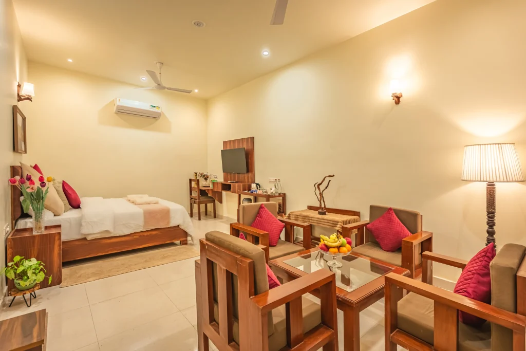 Spacious deluxe room with seating area at Pristine Woods, the Best Resort in Dehradun, featuring a king-size bed, elegant wooden furniture, modern amenities and a warm, luxurious ambience.