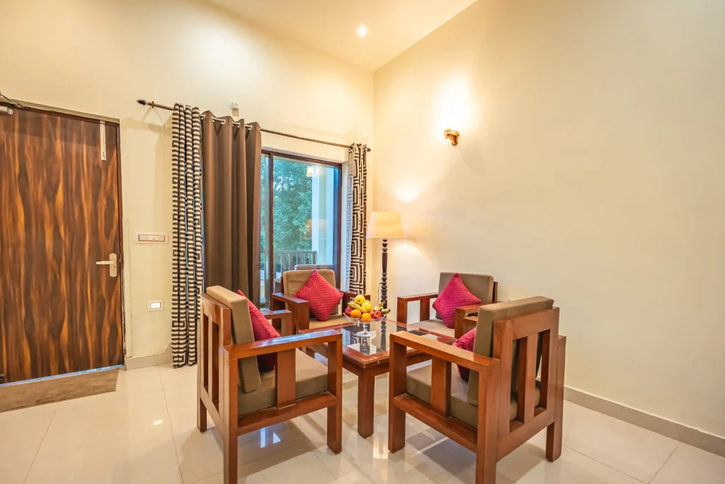Comfortable seating area inside a double deluxe room at Pristine Woods, a Luxury Resort in Dehradun, featuring elegant wooden armchairs, garden-facing glass doors, warm lighting and a relaxing ambience for a premium stay.