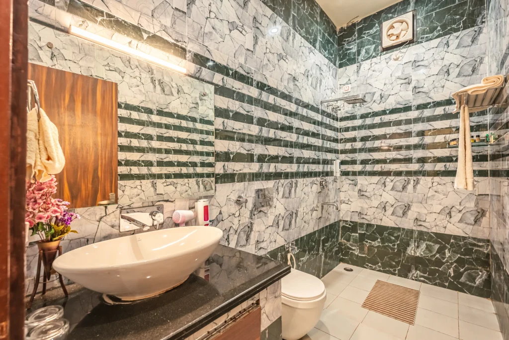 Modern luxury bathroom at Pristine Woods, the Best Resort in Dehradun, featuring premium marble-finish tiles, a stylish washbasin, walk-in shower area and elegant amenities for a comfortable resort stay.