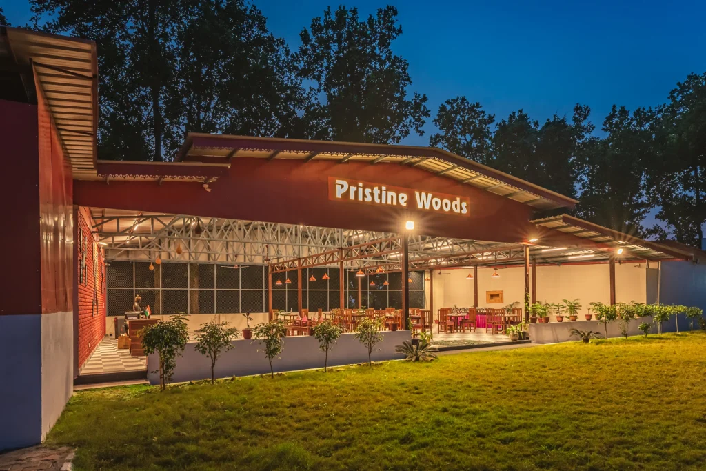 Evening view of Pristine Woods restaurant, part of the Best Resort in Dehradun, showcasing a beautifully lit open-air dining space surrounded by lush greenery, elegant seating and a warm ambience for a memorable dining experience.