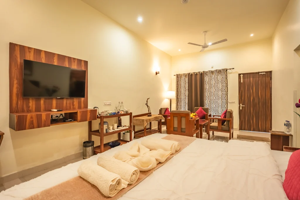Luxury deluxe room interior at Pristine Woods, the Best Resort in Dehradun, featuring a king-size bed, modern TV unit, elegant seating area, garden-facing doors and premium in-room amenities for a relaxing stay.